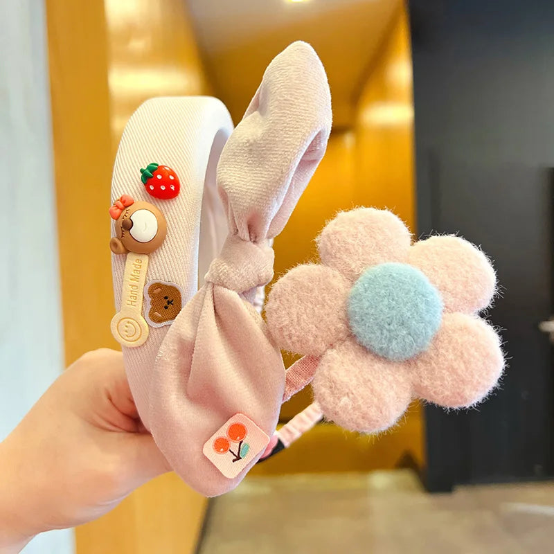 Children's headband with bunny ears and flower accessory held by a hand.