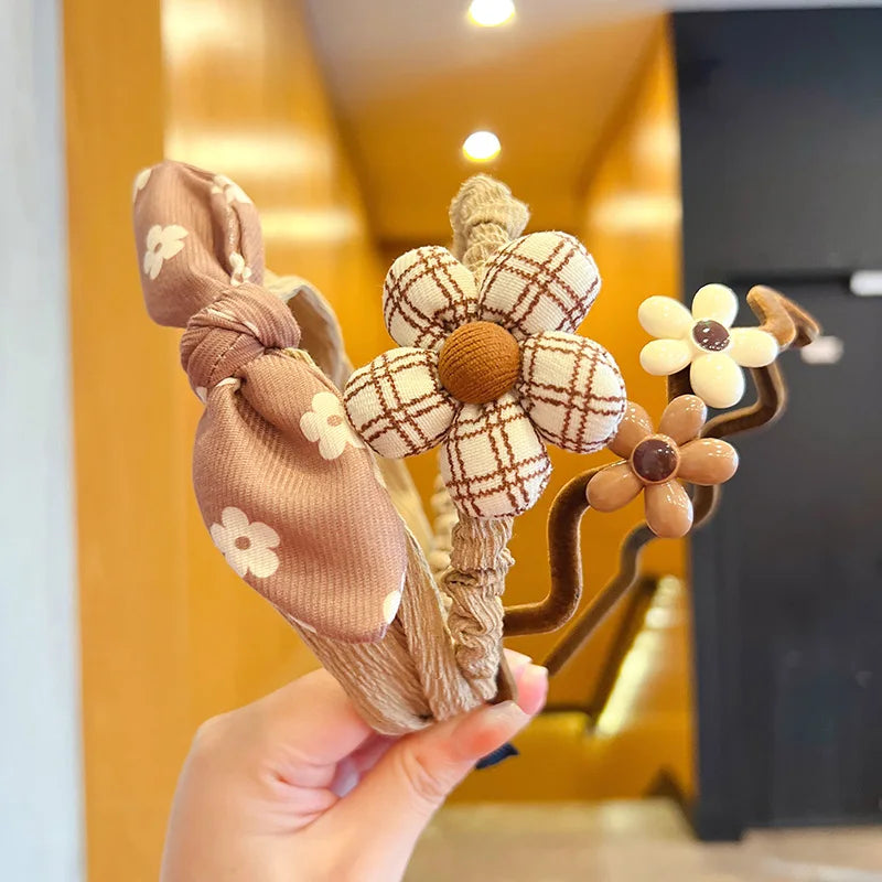 Hand holding a decorative hair bow with floral patterns against a blurred indoor background