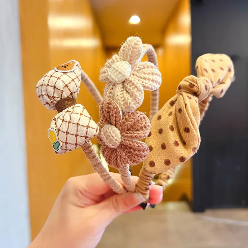 Hand holding three knitted headbands with floral designs against a blurred indoor background