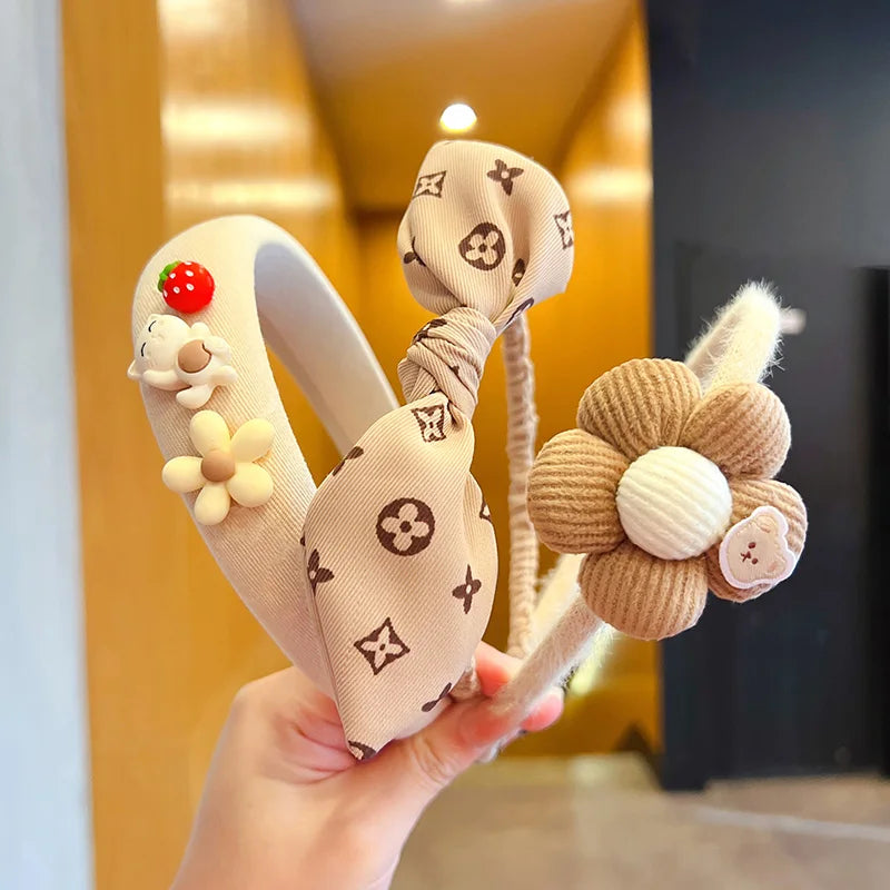 Decorative headbands with floral and animal designs held by a hand against a blurred indoor background.